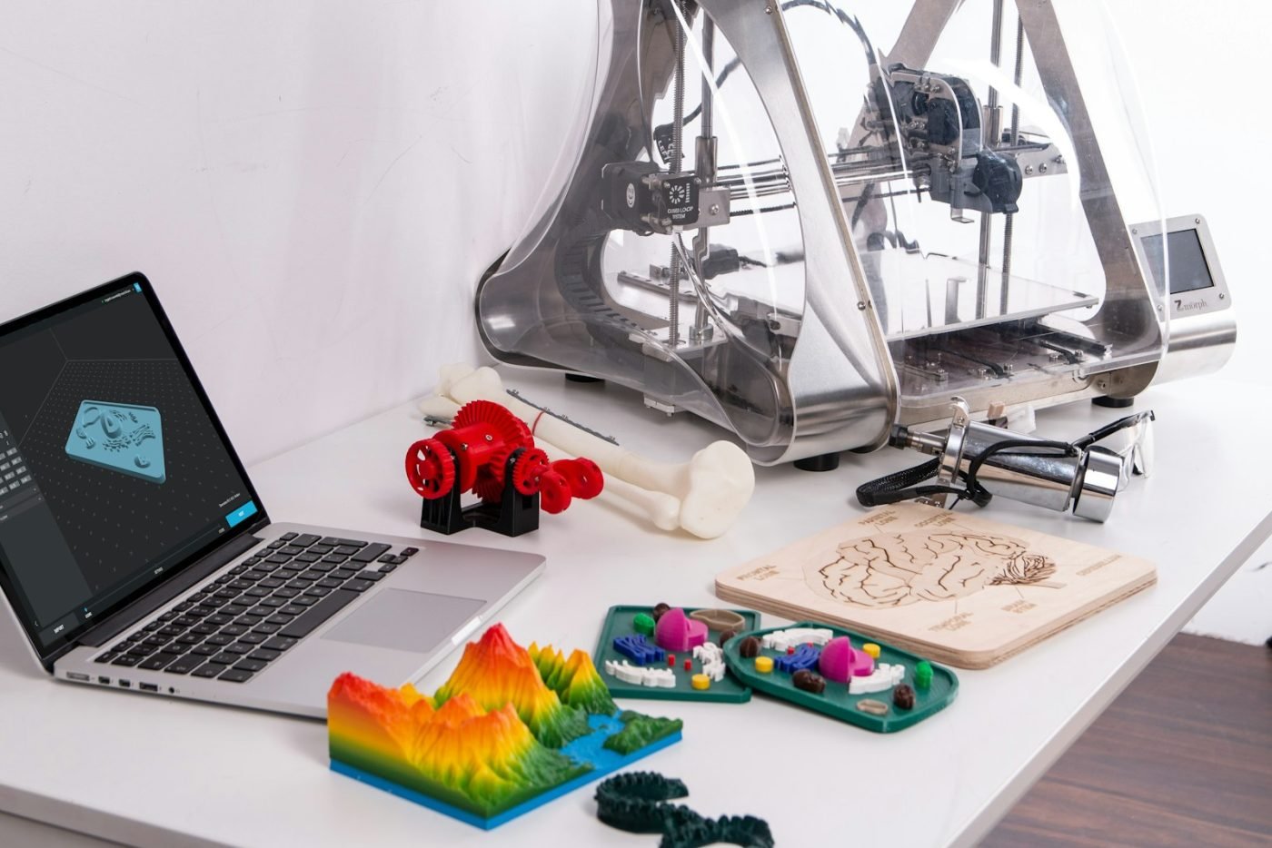 An assortment of 3D printed objects on a desk beside a printer